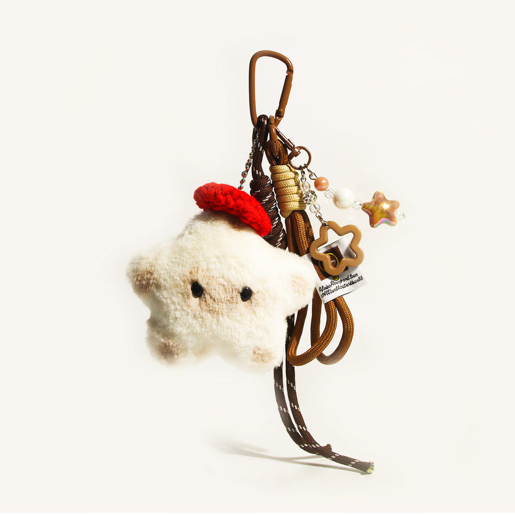 A white plush star-shaped doll with black eyes and a red knitted hat, attached to a brown carabiner with woven cords and decorative elements including a star-shaped acrylic piece and beads.