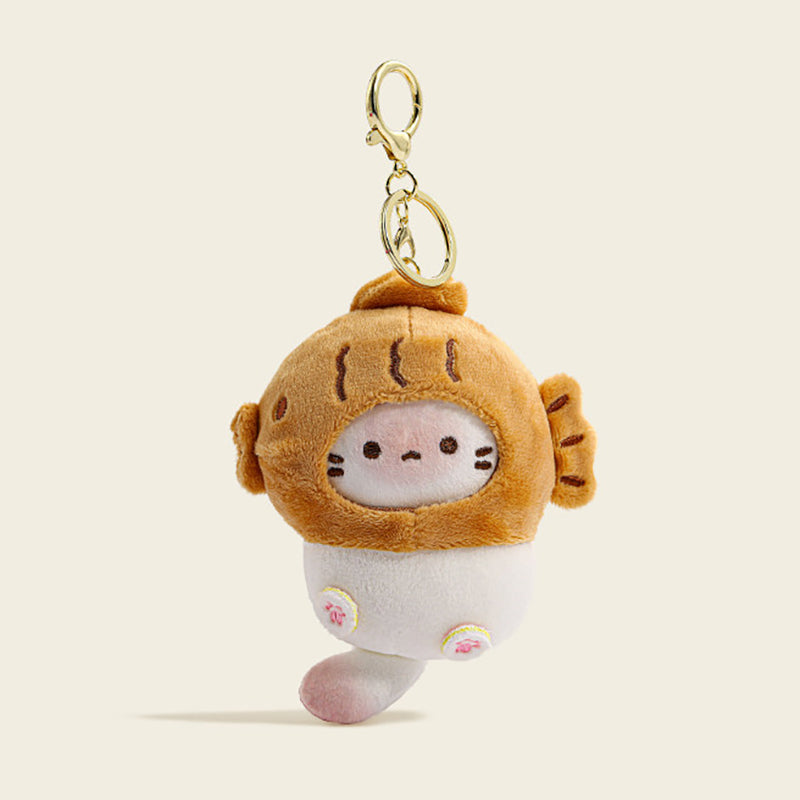 A plush cat bag charm inside a golden-brown taiyaki-shaped costume with embroidered whiskers and pink paw details. It is attached to a gold lobster clasp and keyring, designed as a cute and trendy accessory for bags or keychains.