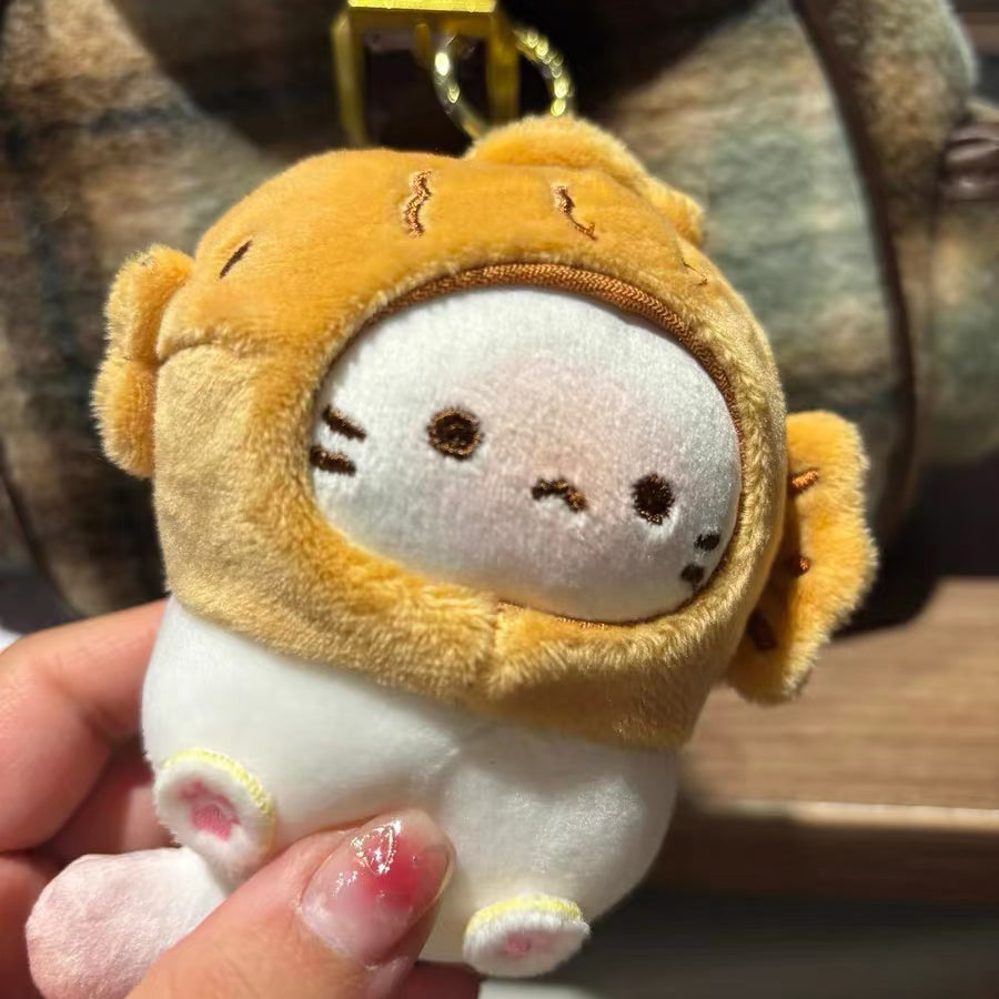 A close-up of a hand holding the white plush cat keychain with a yellow taiyaki hood. The cat's face is visible, showing embroidered black eyes, a small pink nose, and whiskers. The texture of the plush fabric is clear.