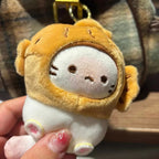 A close-up of a hand holding the white plush cat keychain with a yellow taiyaki hood. The cat's face is visible, showing embroidered black eyes, a small pink nose, and whiskers. The texture of the plush fabric is clear.