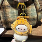 A plush keychain of a white cat wearing a yellow taiyaki-shaped hood with embroidered details, hanging from a brown leather strap on a fuzzy plaid bag. The cat has simple black eyes and whiskers, and a small pink nose.