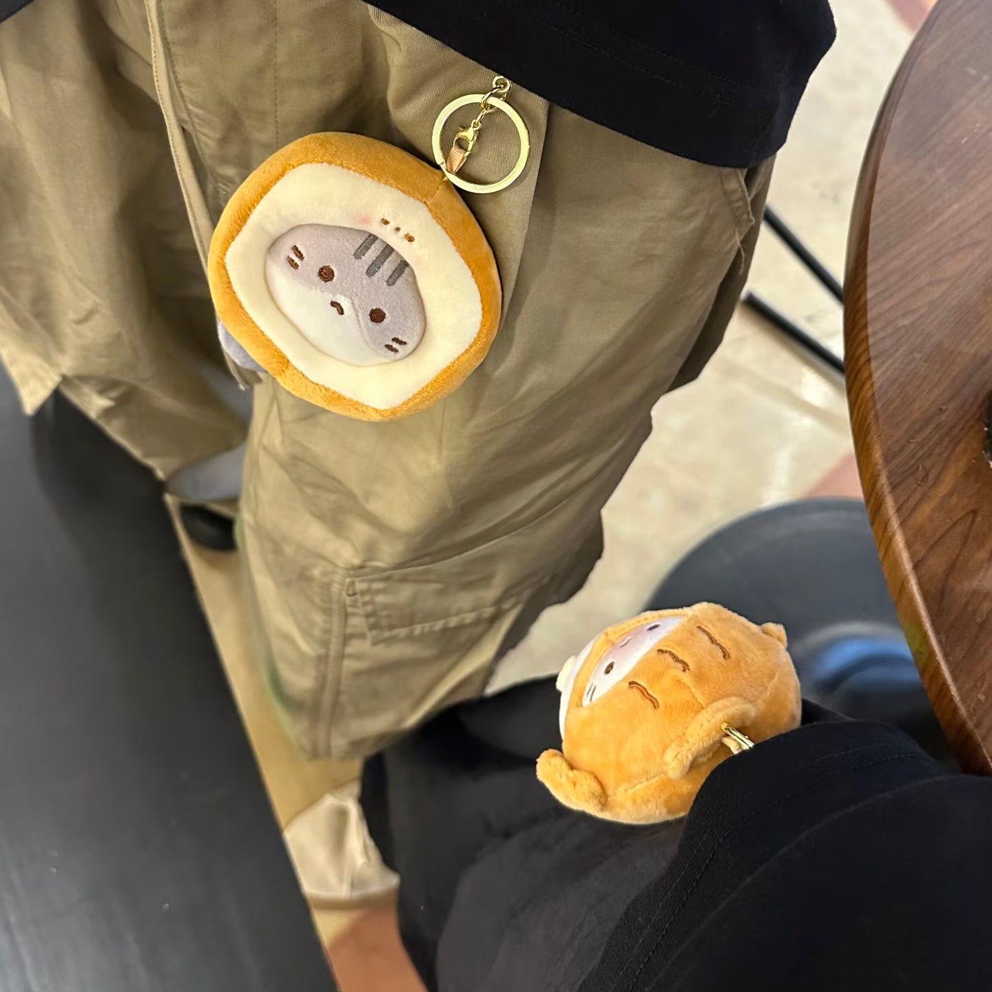Two plush cat keychains with taiyaki hoods are attached to the pockets of a person's khaki cargo pants. One is hanging from the front pocket, and the other is on the side, showing how they can be worn as accessories.