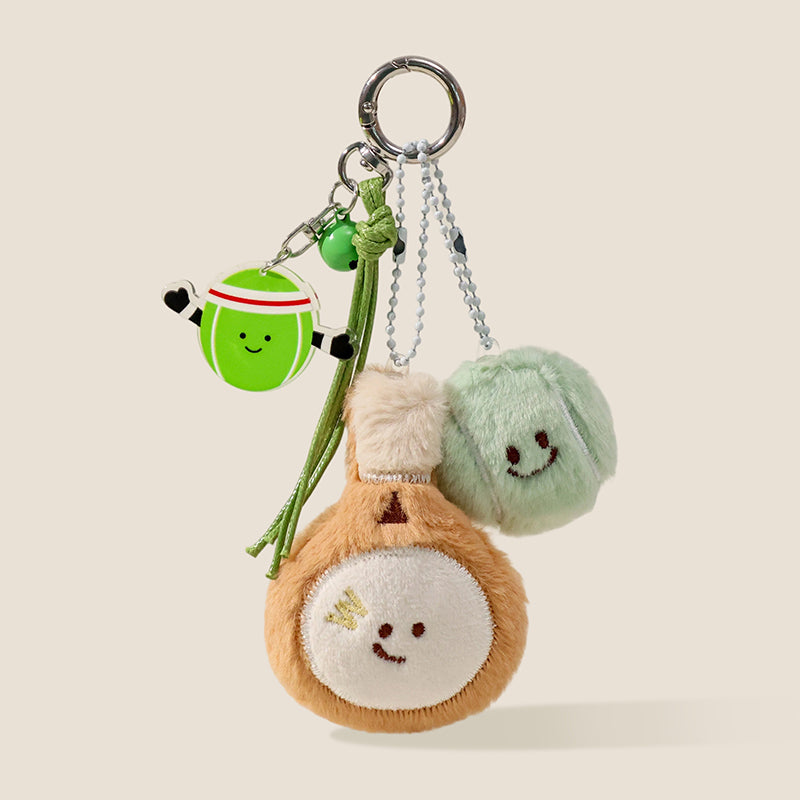 A set of plush keychains featuring a green tennis ball and a brown badminton shuttlecock, both with smiling faces, attached to a keyring with a matching acrylic tennis ball charm and green bell.