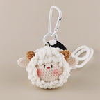 A close-up of a white crocheted sheep plush keychain with brown ears and a smiling face, attached to a white carabiner clip.