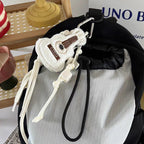 A white plush guitar keychain with brown details hanging from the zipper of a black and grey backpack, featuring a white braided rope strap.