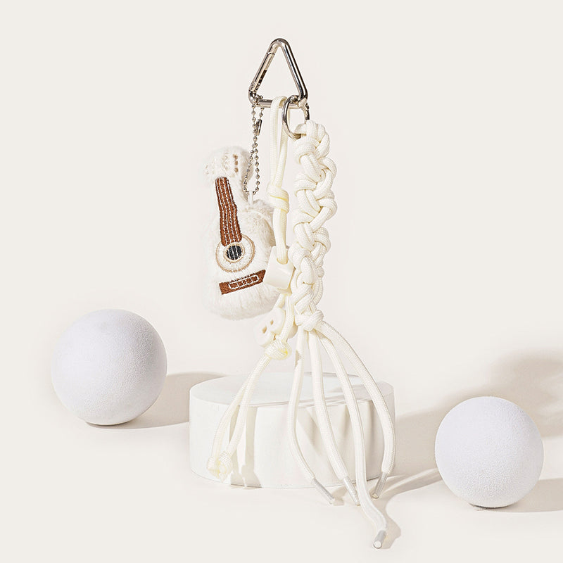 A white plush guitar-shaped keychain with brown embroidered details, hanging from a silver carabiner with a white braided rope strap and white plastic beads.