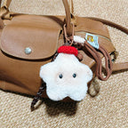 A white plush star-shaped doll with black button eyes and a red knitted hat, attached to a brown leather handbag with a woven strap and a small tag.
