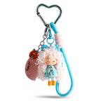 A silver heart carabiner keychain displaying a doll with white curly hair and a light blue dress. It features a light blue braided wrist strap and a dangling comb charm with text.