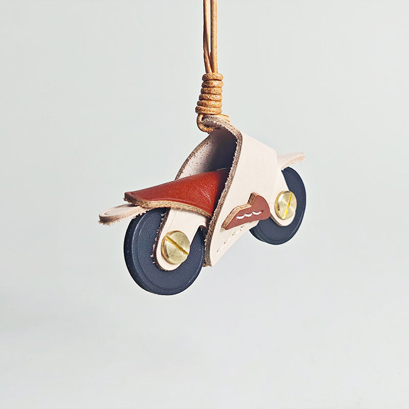 A detailed product shot of a white and maroon leather motorcycle keyring. The image highlights the texture of the leather and the brass hardware used for the wheel axles.
