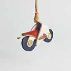A detailed product shot of a white and maroon leather motorcycle keyring. The image highlights the texture of the leather and the brass hardware used for the wheel axles.