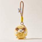 A front-facing view of a yellow fluffy sheep plush keychain with brown spiral horns and a smiling face, attached to a beige cord with a yellow wrap and a small branded tag.